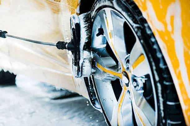 Man washing a car using brush and soap or foam. Manual cleaning modern aloy wheel in selective focus.